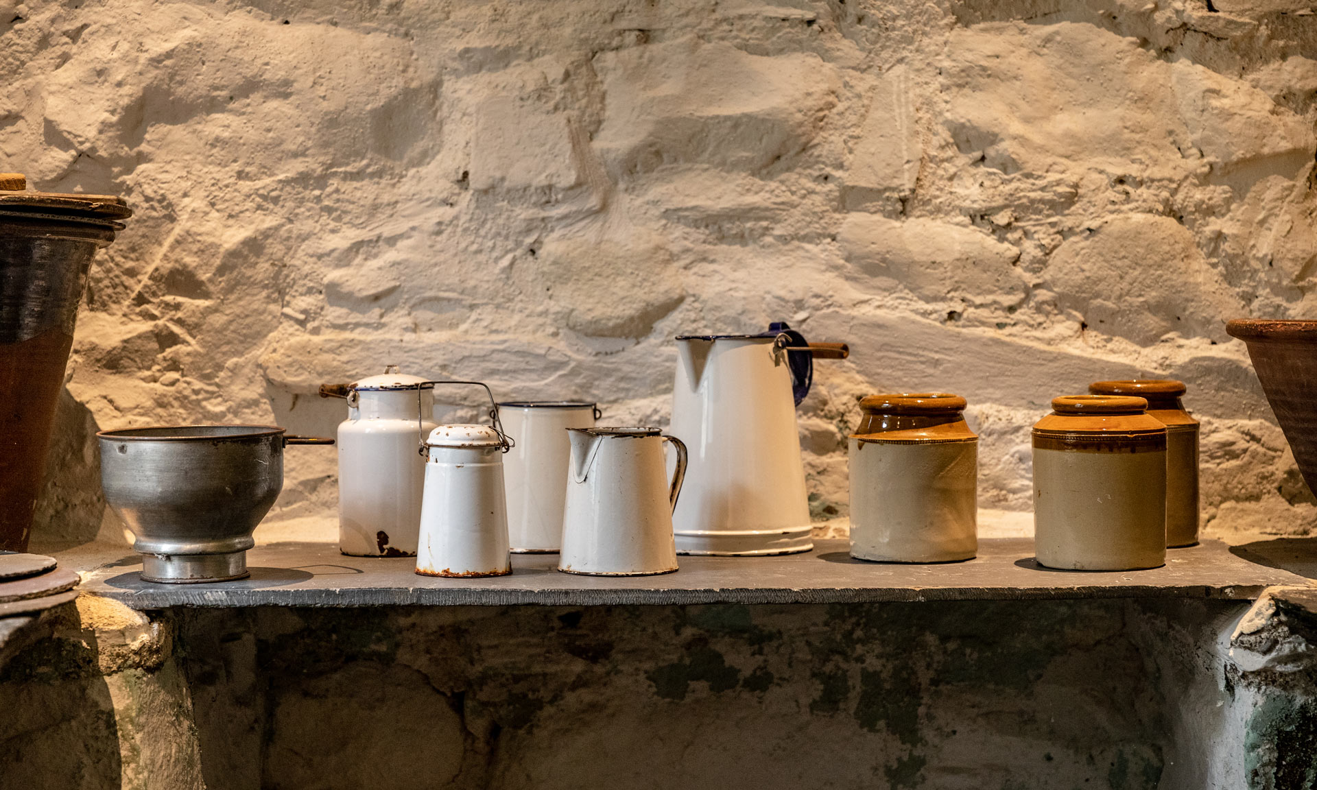 Clay jars and enamel jugs standing on a slate worktop at Yr Ysgwrn's buttery